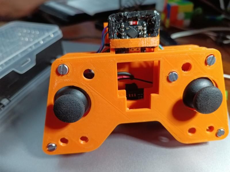 The finished orange 3D-printed remote from the front, with two black thumbsticks and the ESP32-C3 board mounted on top