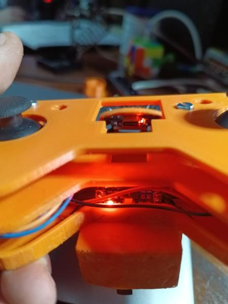 The underside of the remote held in a hand, with a board's red LED glowing inside the case
