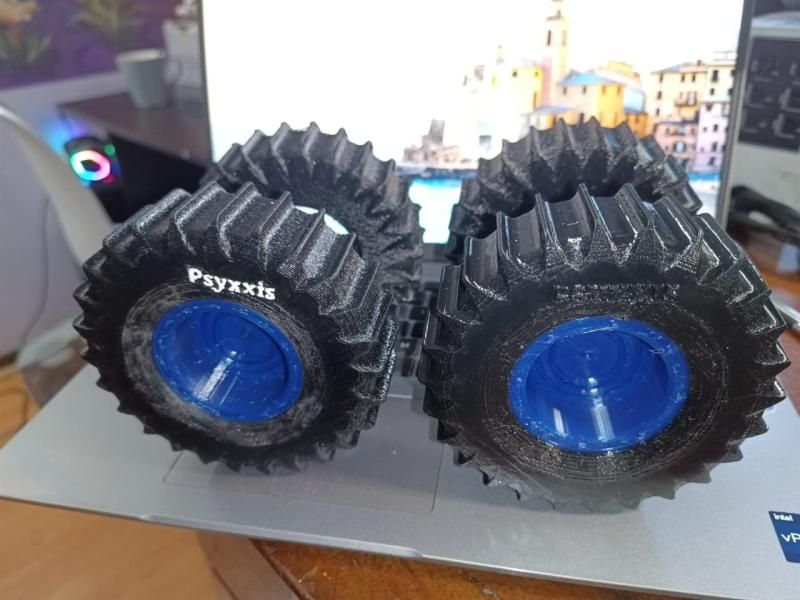 Four finished black TPU tyres on blue rims, stacked in two pairs